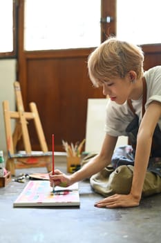 Young gay man artist concentrating on his painting in bright art studio. Art, education and creative hobby concept.