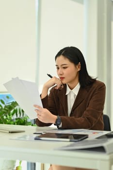 Focused millennial female manager preparing report and analyzing work results at office desk.