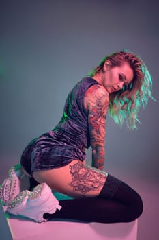 Beautiful young blonde tattoed girl in blue velour booty shorts and t-shirt, she sits on top of big cube, showing off her amazing booty from behind