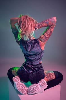 Beautiful young blonde tattoed girl in blue velour booty shorts and t-shirt, she sits on top of big cube, showing off her amazing booty from behind