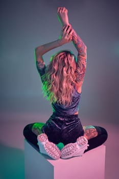 Beautiful young blonde tattoed girl in blue velour booty shorts and t-shirt, she sits on top of big cube, showing off her amazing booty from behind