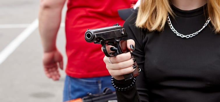 A young girl with a gun in her hands. Makarov pistol in young hands with black manicure.