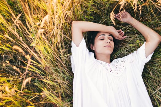 Conceived Beautiful young woman lying in the grass, wearing a white dress. Nature, summer holidays, vacation and people concept