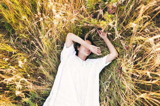 Conceived Beautiful young woman lying in the grass, wearing a white dress. Nature, summer holidays, vacation and people concept