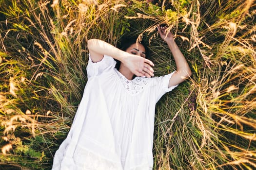 Conceived Beautiful young woman lying in the grass, wearing a white dress. Nature, summer holidays, vacation and people concept