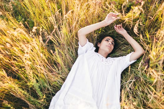 Conceived Beautiful young woman lying in the grass, wearing a white dress. Nature, summer holidays, vacation and people concept