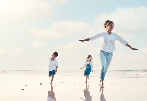 Mother, son and daughter on the beach to dance together while outdoor for travel or vacation in summer. Sunset, family or children and a woman having fun with her kids on the coast by the ocean.