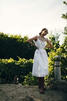 Portrait of a beautiful girl in a white dress in the garden. Burnette beautiful natural girl with in a white dress in nature, on the street, in the garden by a tree, with makeup and hairstyle