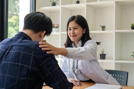 Asian female doctor giving hope and encourage to stressed man patient at hospital. Smiling doctor woman touching on patient shoulder to support take care and helping . Supported and Encouraged.