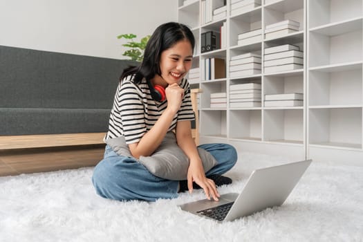 Cute teen woman asian is doing using laptop at home on the floor. She is excited and smiling.