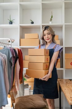Portrait of Asian woman sell clothing online and looking at camera. Attractive beautiful young business woman standing hold the box confident in house.