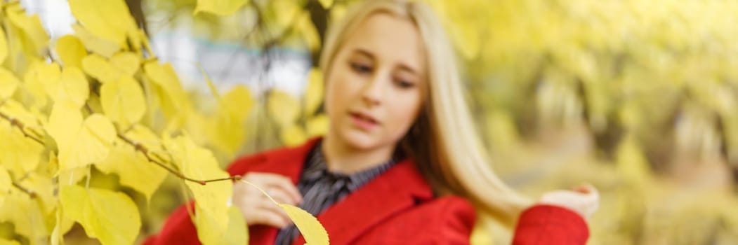 A young blonde woman walks around the autumn city in a red coat. The concept of urban style and lifestyle.