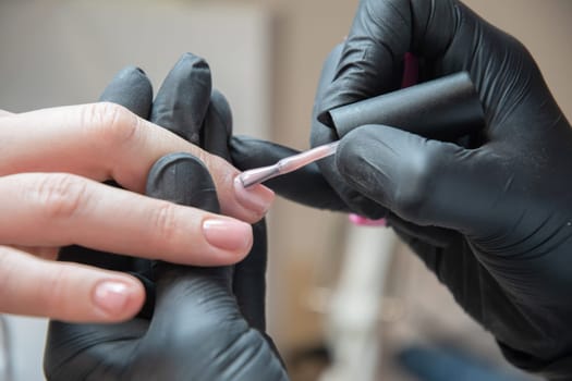 a master does a manicure to a client in a beauty salon and covers her nails with pink varnish. High quality photo