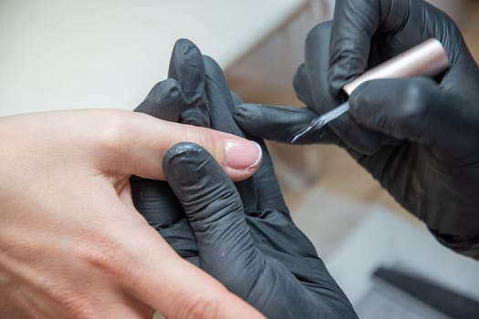 a master does a manicure to a client in a beauty salon and covers her nails with pink varnish. High quality photo