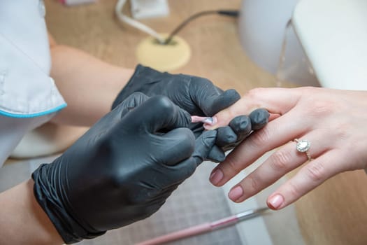 a master does a manicure to a client in a beauty salon and covers her nails with pink varnish. High quality photo