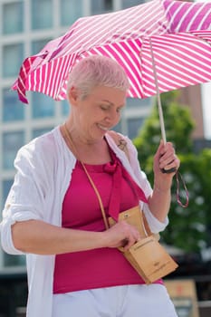 middle-aged woman with a short haircut with an umbrella protecting from the scorching sun is looking for something in her handbag, and smile, High quality photo