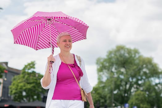 middle-aged woman with a short haircut with an umbrella protecting from the scorching sun looks at the camera and laughs, High Quality Photo