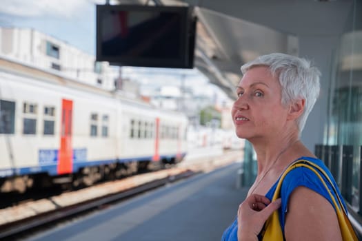 Active gray-haired woman waiting for a train on the platform of the city station, travel, tourism, public transport, Middle-aged woman leading a healthy lifestyle, High Quality Photo