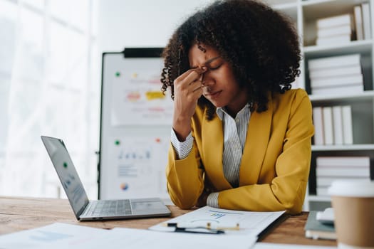 Burnout American African business woman in stress works with many paperwork document, migraine attack, Freelance, work at office.