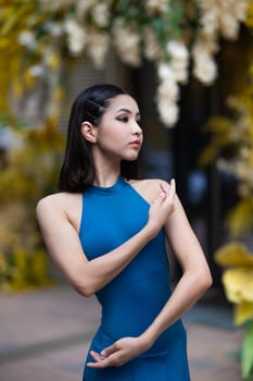 Beautiful Asian ballerina posing against the backdrop of a building decorated with flowers