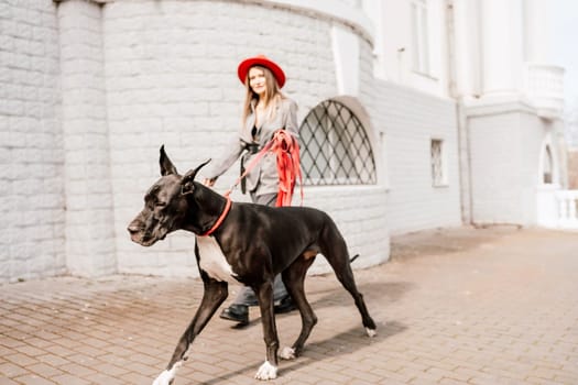 A photo of a woman and her Great Dane walking through a town, taking in the sights and sounds of the urban environment.