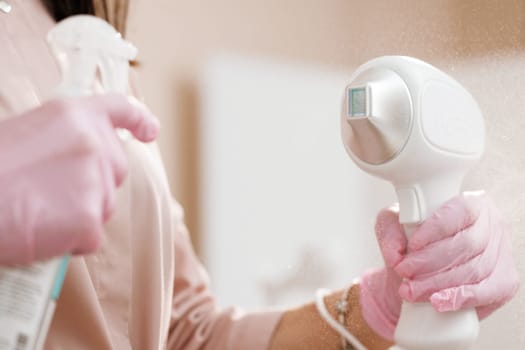 Female cosmetologist hands holding laser device. Close up of female beautician in sterile gloves using diode laser hair removal machine. Esthetician preparing equipment for epilation procedure.