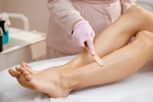 Close up of cosmetologist in sterile gloves applying ultrasound gel on female leg before epilation. Esthetician preparing woman skin for laser hair removal treatment in cosmetology clinic.