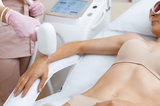 Beautician hands performing laser hair removal procedure. Pink gloves hold the epilation device, the hands of the doctor remove hair on hands with a laser device. Laser hair removal treatment.