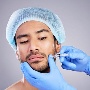 Hands, face and plastic surgery with a man in studio on a gray background for a botox injection. Needle, beauty and transformation with a male customer in a clinic for antiaging filler or cosmetics.