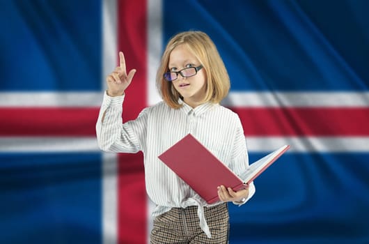 A girl with a book in her hand shows a gesture - attention on the background of the flag of Iceland. Education concept.