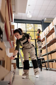 Warehouse manager scanning cardboard box barcode using store scanner, working at merchandise shipping for customers. Supervisor wearing headphones listening music during storehouse inventory