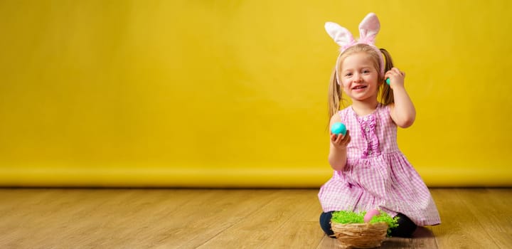Toddler blonde happy girl with bunny ears and basket of eggs for Easter