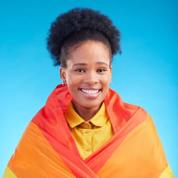 Pride, flag and portrait of black woman in studio for gay, rights and lgbtq lifestyle on blue background. Rainbow, freedom and face of lesbian African female happy, smile and confident with sexuality.