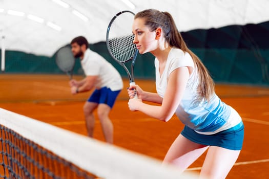 Pair of tennis players, man and woman waiting for service at indoor court