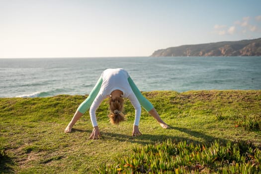 Senior woman doing yoga pose on ocean shore. Retired female practicing yoga and flexibility. Sports activities in nature. Wellness concept, yoga exercise