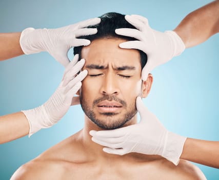 Face, hands and plastic surgery with a nervous man in studio on a blue background for beauty enhancement. Aesthetic, botox and change with a young male patient eyes closed in a clinic for skincare.