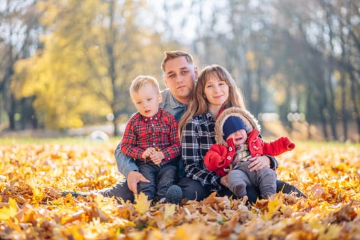 A young family sits in the park on a leafy, sunny autumn day