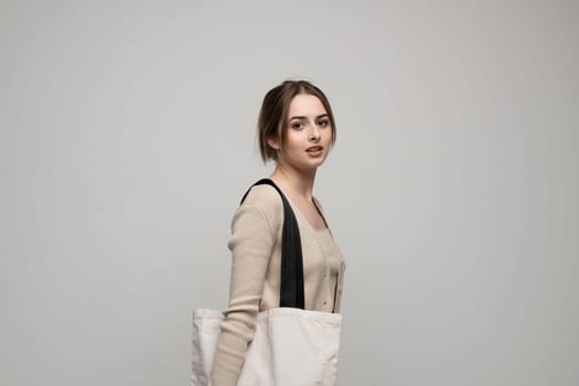 Cheerful millennial woman with a white eco bag standing over white studio background. Lady holding shopper handbag. Fashion and ecology concept, Selective Focus. No more plastic