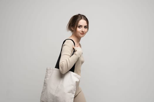 Cheerful happy woman in a beige costume with white cotton bag in her hands. Mockup and zero waste concept. Eco friendly lifestyle. Reuse, recylce, zero waste, No more plastic