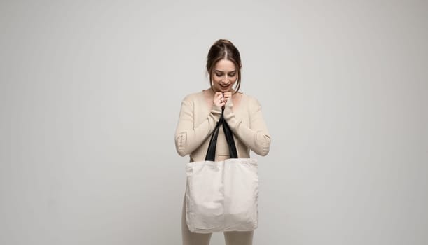 Young happy and excited woman in beige costume with white cotton bag in a hand. Mockup and zero waste concept