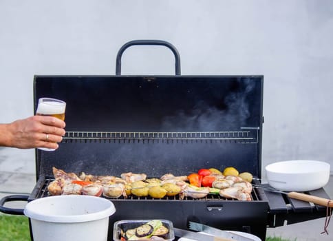 men hold beer in their hands on the background of the grill, vegetables and meat. Selective focus. Nature