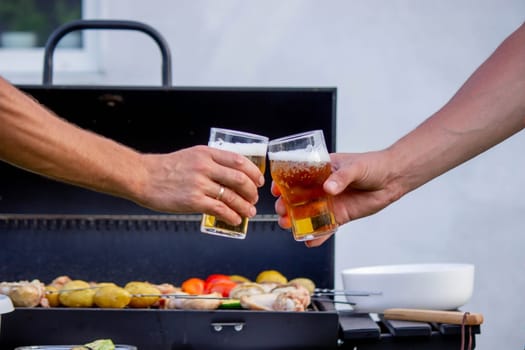 men hold beer in their hands on the background of the grill, vegetables and meat. Selective focus. Nature