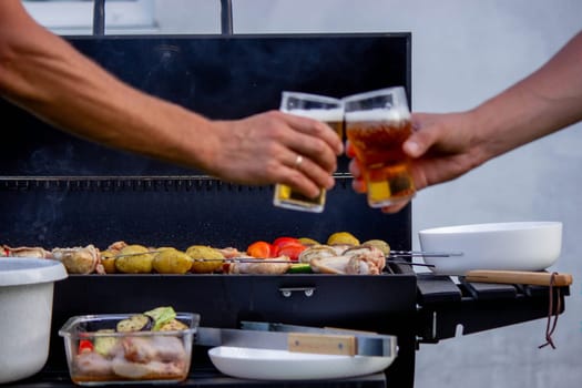 men hold beer in their hands on the background of the grill, vegetables and meat. Selective focus. Nature