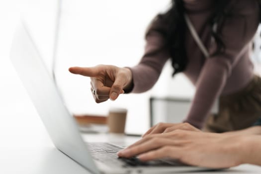 Businesswoman working on laptop computer on office table with person teaching.