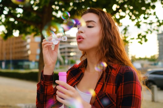 Red haired girl in a red plain shirt blowing air bubbles standing in the street.