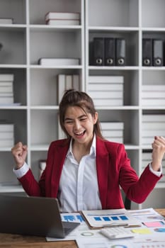 Beautiful Asian businesswoman celebrate while using laptop at office and showing delight. Startup small business and successful concept.