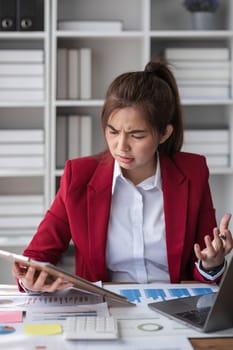 Young Asian businesswoman working on laptop computer use clipboard stressed has a headache and thinks hard from work at the office.