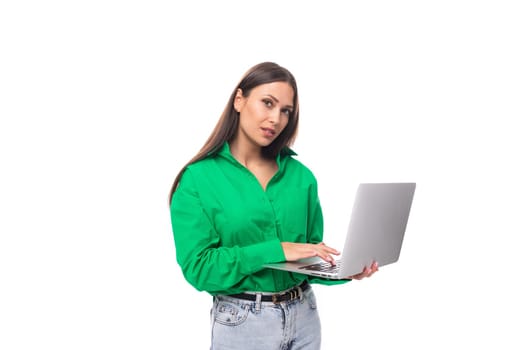 young european brunette woman with brown eyes in green blouse works online using laptop.
