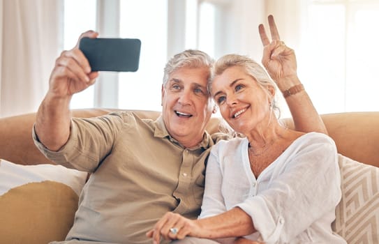 Happy senior couple, peace sign and selfie in relax on living room sofa for photograph, memory or vlog at home. Elderly man and woman smile for picture, photo or social media on lounge couch together.