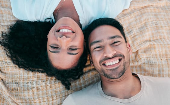 Portrait, picnic and smile with a couple on a blanket from above, lying down on the ground while on a date. Face, love or happy with a man and woman bonding together for romance on valentines day.